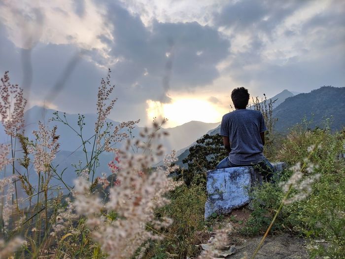 Rear view of man sitting on land against sky