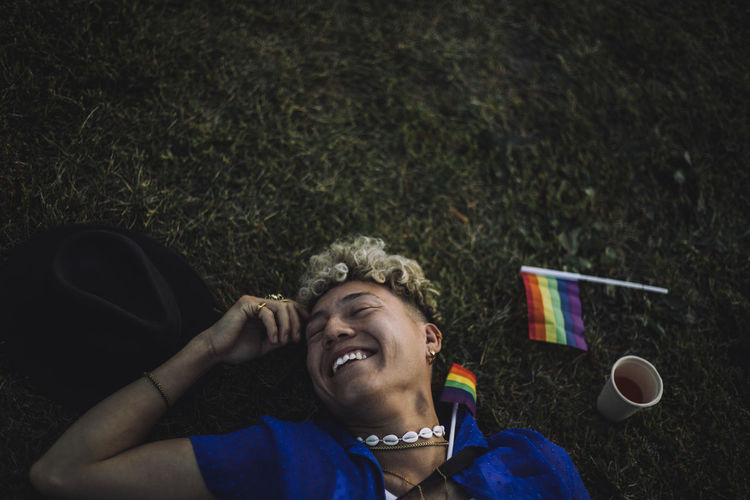 Happy young men with eyes closed lying by rainbow flag on grass