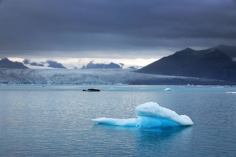 Scenic view of iceberg in lagoon against sky