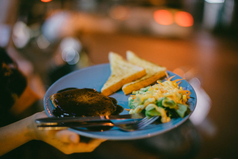Cropped image of hand holding food in plate during night outdoors