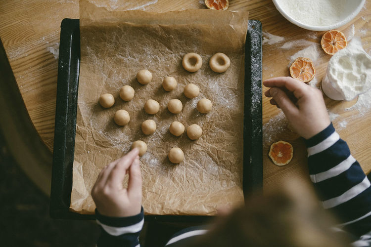 Cropped hands of woman preparing dough balls in baking sheet on table at home