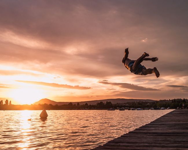 Man jumping in lake against sky during sunset