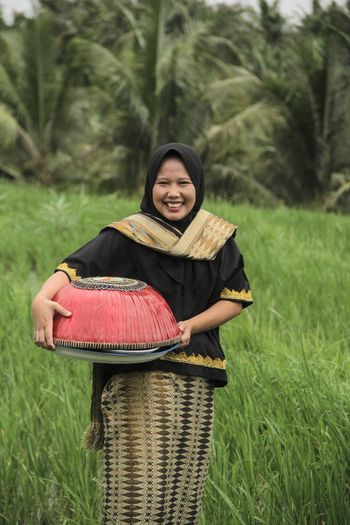 Portrait of smiling young woman using laptop while sitting on field
