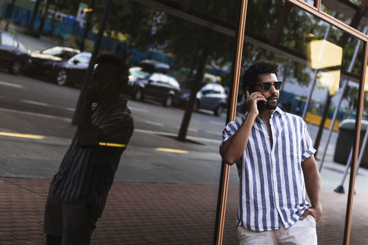 Confident man talking on mobile phone while standing against building