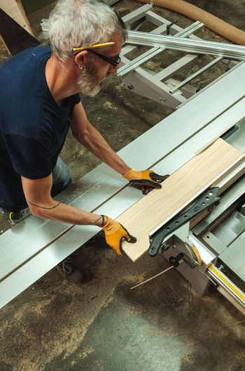 Craftsman using machinery while working on wooden planks in workshop