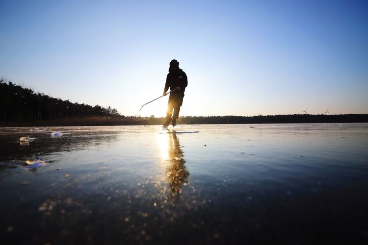 Silhouette man ice skating on frozen lake against sky