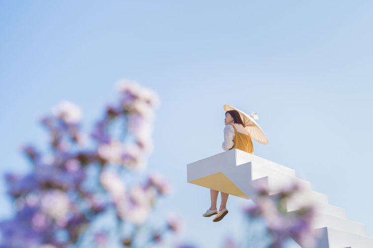 Asian woman relax and hold umbella on white stair in flower garden on springtime vacation