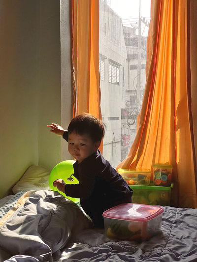 Boy looking away while sitting on bed at home