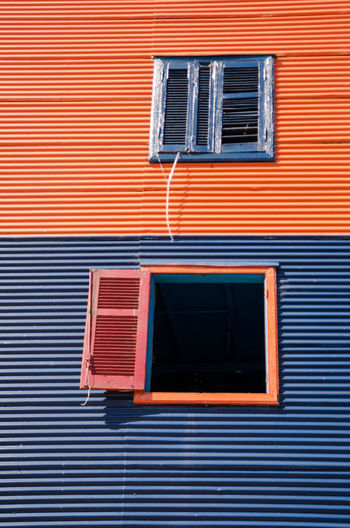 Low angle view of shuttered windows on two toned colourful corrugated iron building exterior. 