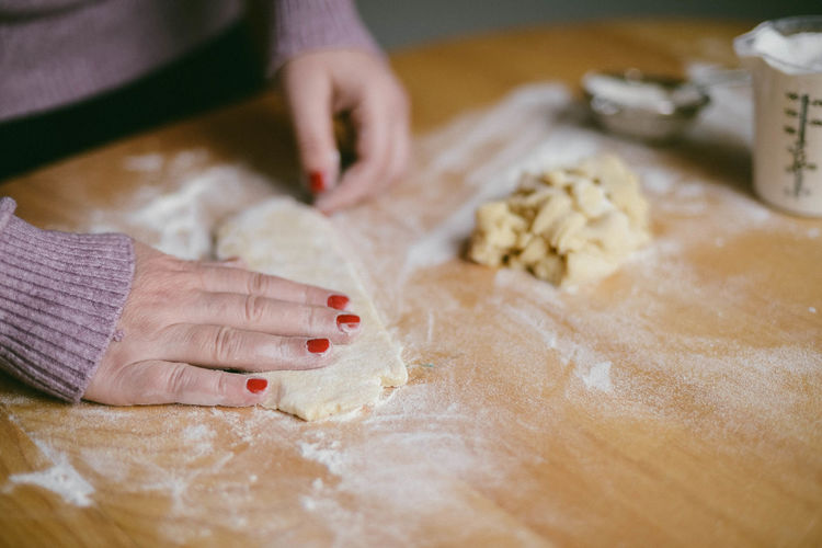Midsection of woman preparing dough at table in kitchen