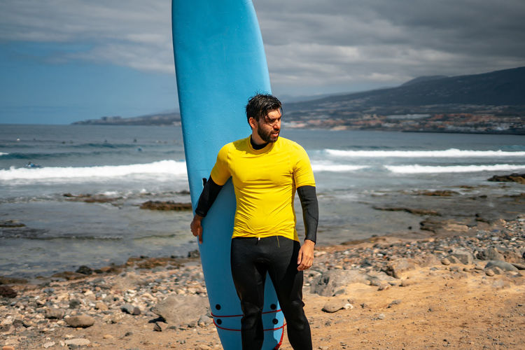Man with surfboard standing at beach against sky