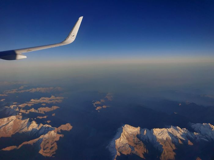 Aerial view of aircraft wing over mountains against blue sky