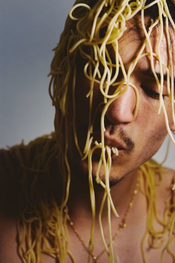 Close-up of young man covered in spaghetti against wall
