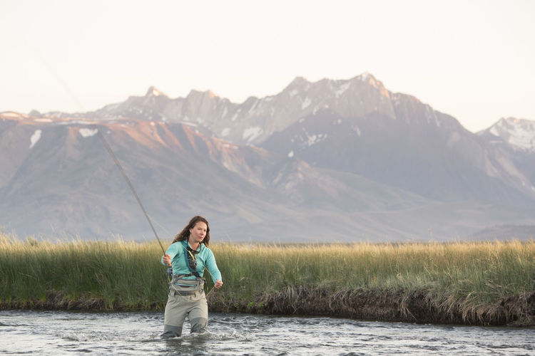 Young woman fly-fishing in owens river against mountains