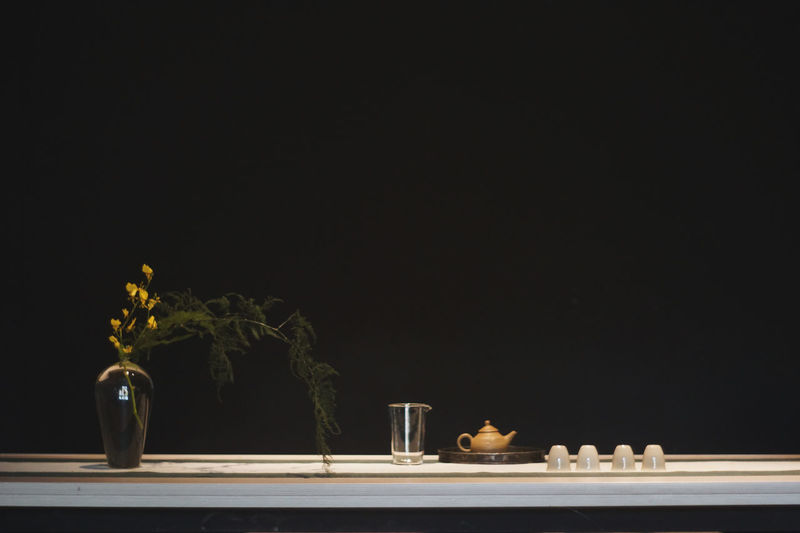 Close-up of vase and crockery on table against black background