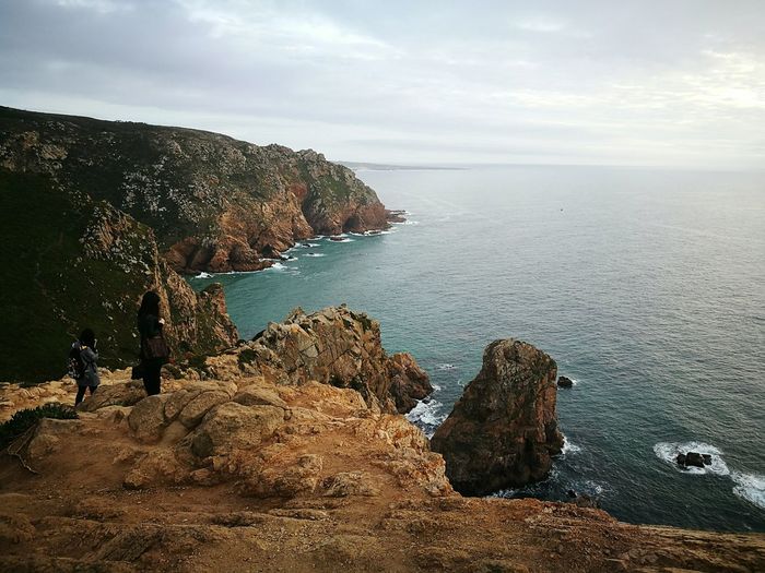 Rear view of women standing on rock formation while looking at sea in cabo da roca