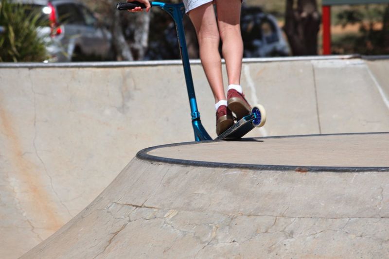 Low section of person riding push scooter at skateboard park