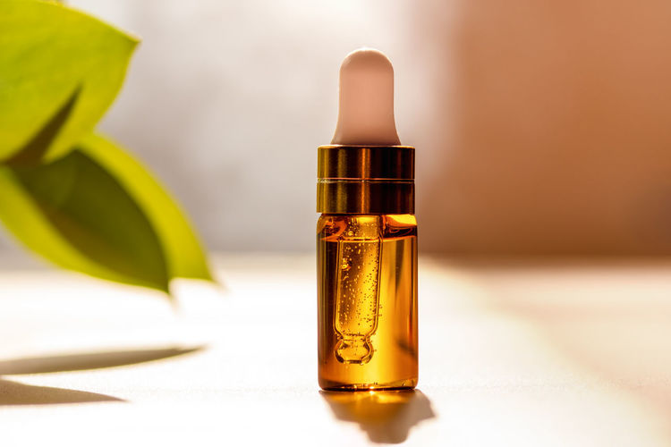 Cosmetic glass dropper bottle with oil, serum or fruit peeling in the sunlight. green eucalyptus