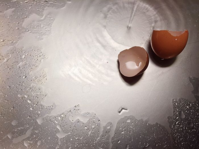 Directly above shot of eggshells by water falling on metallic table