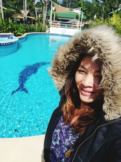 Portrait of smiling woman wearing warm clothing by swimming pool during sunny day