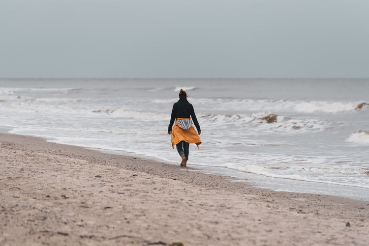 Rear view of woman walking at beach against sky