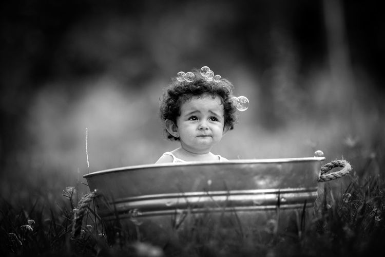 Baby girl sitting in bucket on field