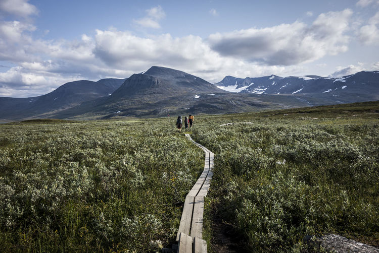 Scenic view of land and mountains against sky with people hiking