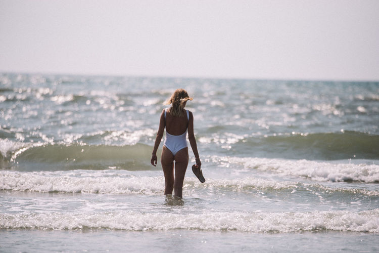 Rear view of young woman wearing one piece swimsuit standing at beach