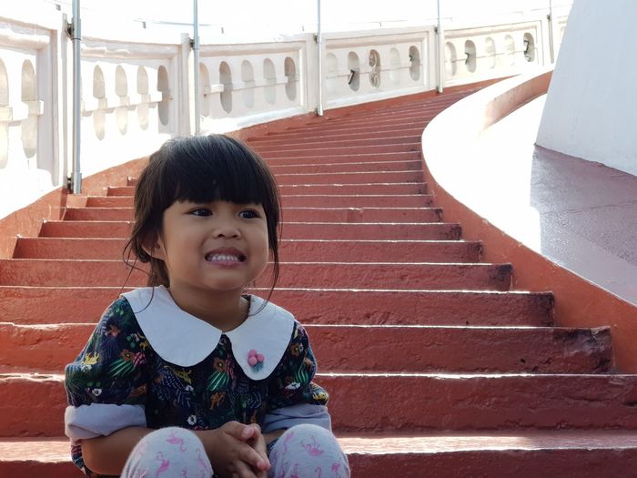Cute girl with clenching teeth sitting on staircase outdoors