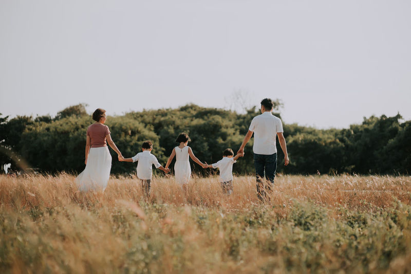 Rear view of family walking on field against sky
