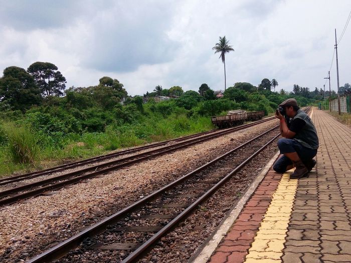 Side view of man photographing while crouching at railroad platform