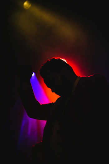 Silhouette man holding illuminated light against sky at night