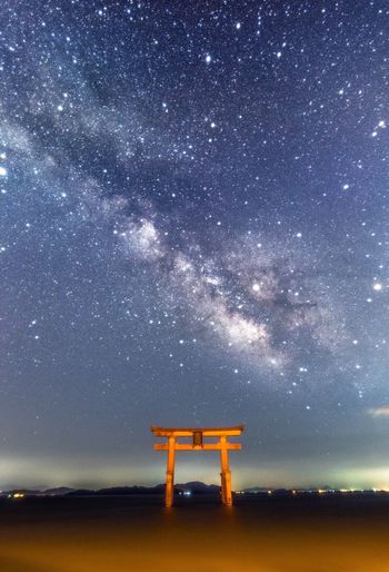 Low angle view of stars over torii gate and river against sky at night