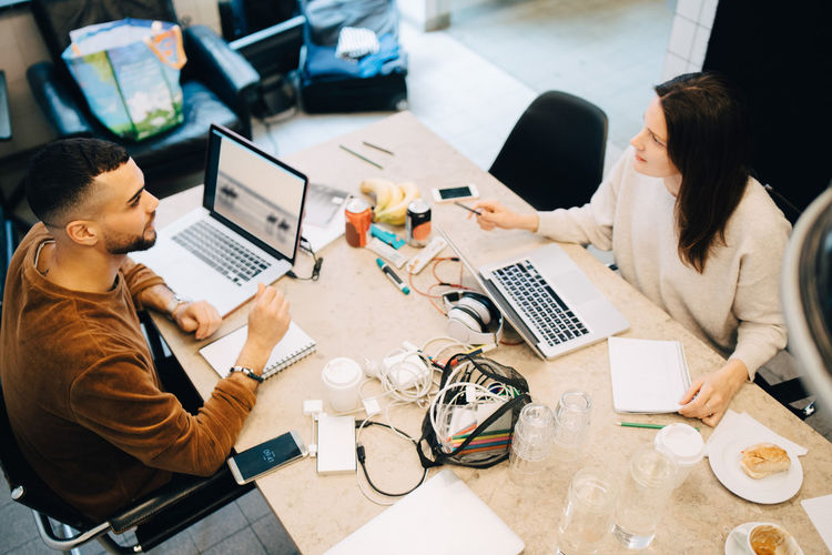 High angle view of male and female programmers discussing while sitting at desk in creative office