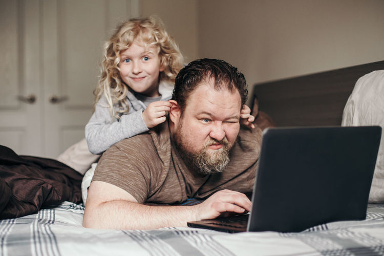 Work from home with kids children. father working on laptop in bedroom with child daughter on back
