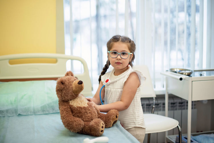 A girl in a hospital room plays doctor with a teddy bear. fun for the child while in the hospital