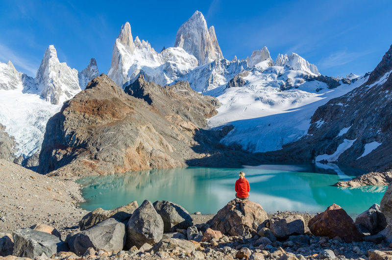 Rear view of person sitting on rock against sky during winter