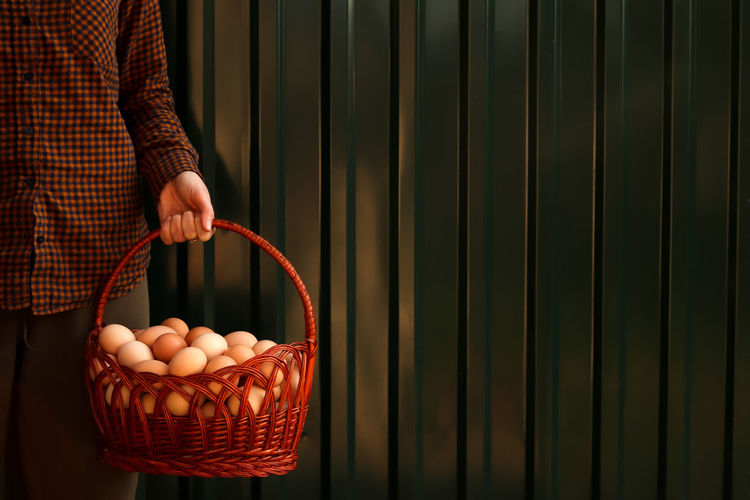 Many eggs in basket. young female farmer holding whole basket of brown organic eggs on modern green