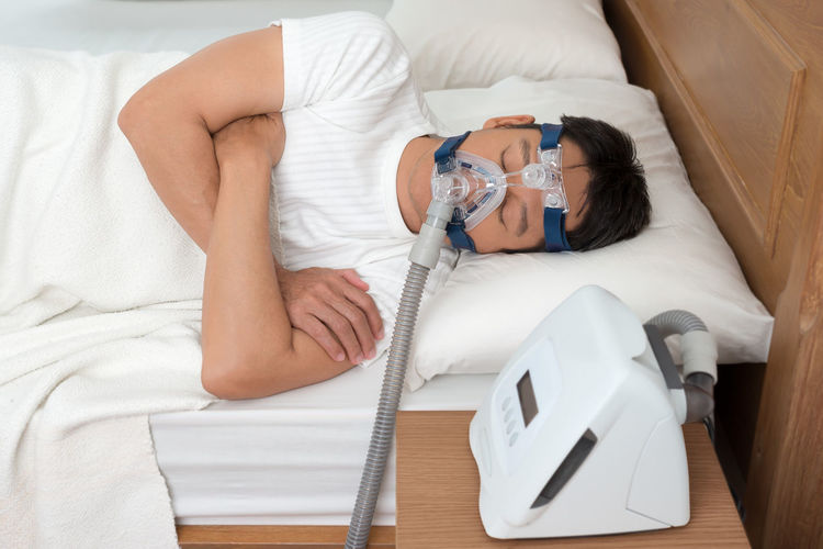Man wearing cpap mask while suffering from sleep apnea on bed at home