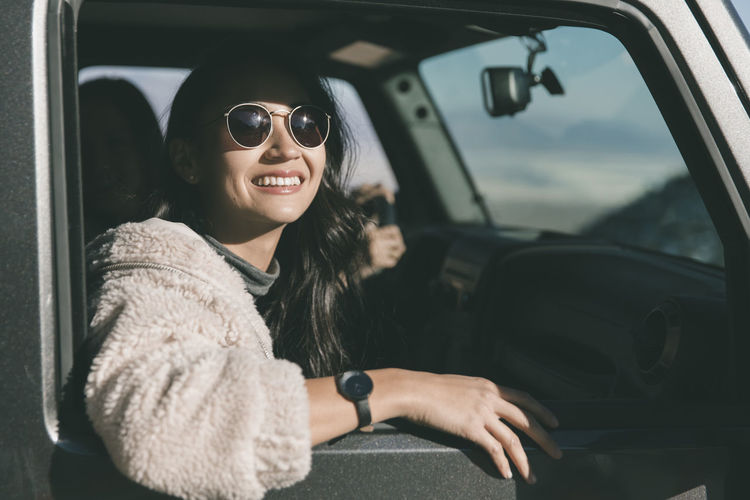 Cheerful young woman wearing sunglasses while sitting in off-road vehicle at desert during sunny day