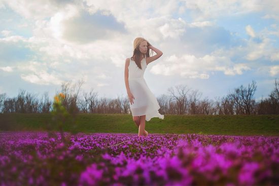 Girl with hand in hair looking away while walking on field against cloudy sky