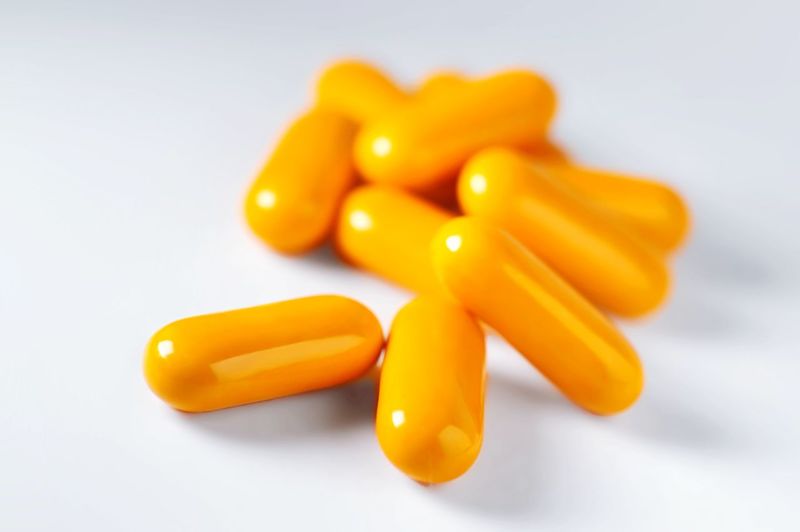 Orange vitamin pills on white surface