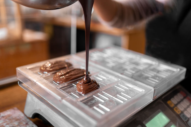 Cropped unrecognizable person in apron and gloves filling plastic mold on digital scale with liquid chocolate during work in confectionery in daytime person
