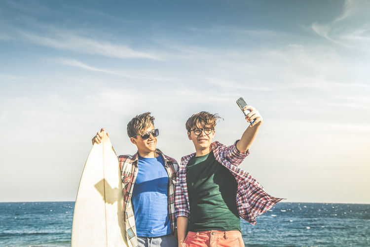 Two young boy on the beach near sea taking picture with phone men on vacation video chat with friend