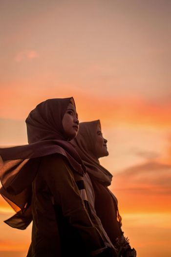 Low angle view of women wearing hijabs looking away against sky during sunset
