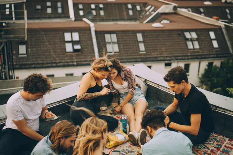 Male and female friends using smart phones while sitting on terrace during party