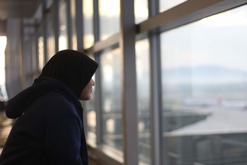 Woman wearing hijab while looking through window at airport