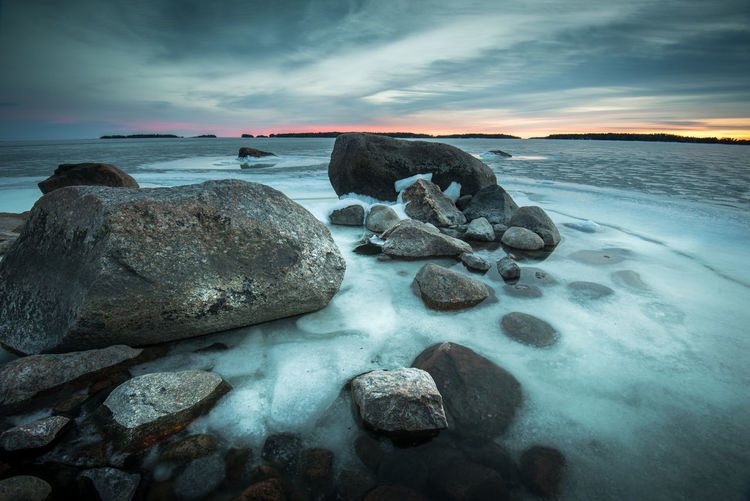 Rocks in frozen sea during sunset