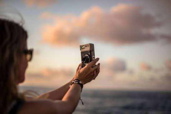 Portrait of woman photographing sea at sunset