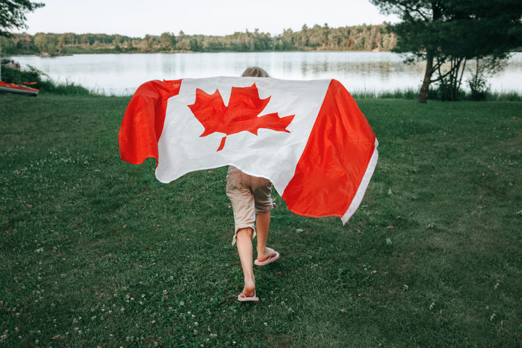 Girl wrapped in large canadian flag by muskoka lake in nature. canada day celebration outdoors. 